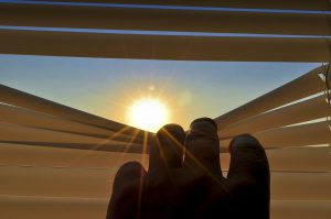 man's hand peeping through the blinds at the sun.