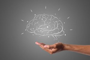 persons hand over a white drawing of a brain with a gray background.