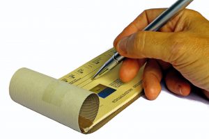 Caucasian hand holding a pen on an open checkbook.
