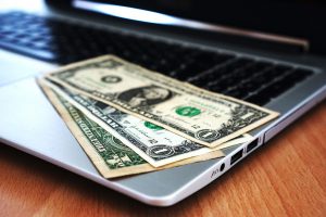 dollar bills sitting on top of a laptop keyboard.