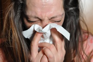 middle aged caucasian woman blowing her nose into a tissue.