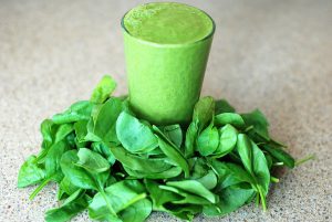cup filled tot he top with green smoothie with spinach laying all around the cup.
