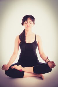 caucasian woman in tank top and yoga capris sitting in a meditation position with hands on knees. 