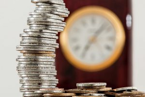 coinds stacked up with a clock in the background blurred.