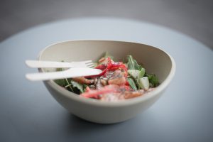 white bowl with salad inside of it and a fork and knife laying on top.