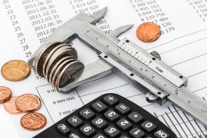 calculator on a table with papers with a lot of numbers and coins being pinched with wrench