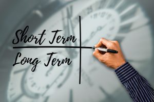 person drawing a cross with short term words over long term.