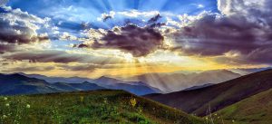 sun shining through clouds outdoors in a green field.