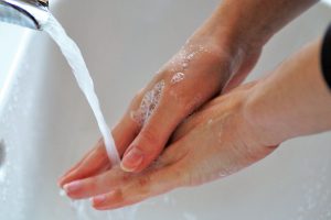 caucasian hands with soap on them washing themselves under a running faucet.