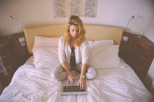 Caucasian woman sitting in her bed with a laptop open in front of her.