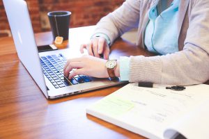woman sitting at a desk with her hands over a laptop and notebook next to the laptop.