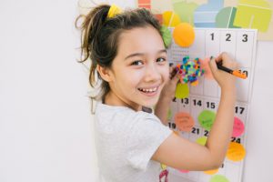 little girl amiling with a pen in her hand in front of a calendar