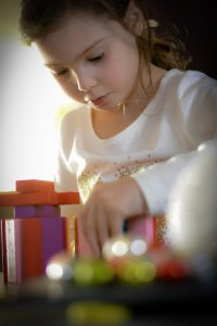little caucasian girk building blocks on a table.