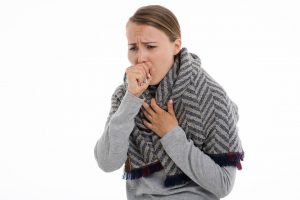 caucasian woman with scarf over her shoulders coughing into her right hand.