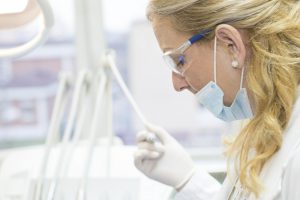 caucasian woman with a face mask on and white coat with a swab in her hand and googles on.