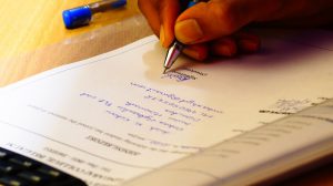 hand with a pen in it writing down on a piece of paper.