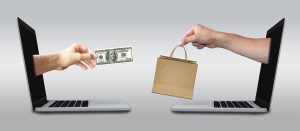 hand out of one laptop screen with money handing it to another hand that is outside a laptop screen with a brown bag.