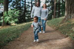 african american man with his arm over a caucasian woman with both watching a little boy running ahead of them.