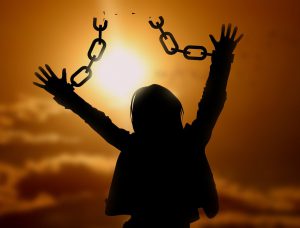 silhouette of a omwan with her hands in the air and broken chains