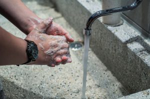 caucasian hands full of soap rubbing together near an open faucet.