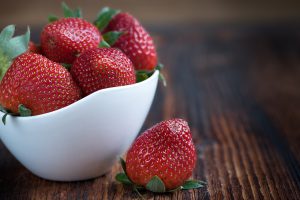 white cup full of strawberries with one on a table.