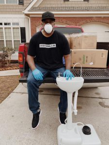 man with a mask on sitting on the back of a pickup truck touching a white sink.