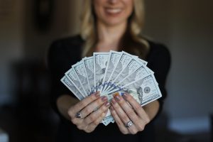 caucasian woman with blonde hair blurred in the backgroun holding 100 dollar bills in her hands