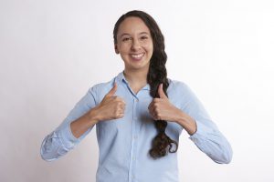 young caucasian woman in light vlue button up with side braid and both thumbs up.