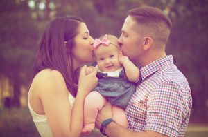 caucasian couple hlding a baby girl in the middle while both are kissing each cheek