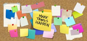 bulletin board with many post notes and a big one in the middle that says "make things happen"