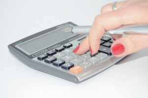 caucasian womans hand holding a pen in her hand pressing a number on a calculator