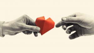 one hand with a red paper heart giving it to another hand