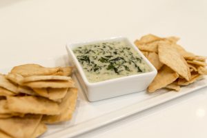 spinach artichoke dip in a bowl with chips around it