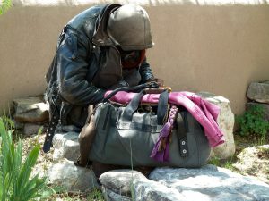 homeless person sitting outside with a black bag full of clothes