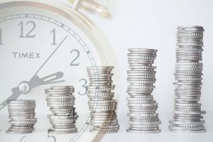 piles of coins going up in range with a clock in the background