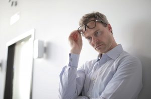 caucasian man with a white button up lifting his glasses above his eyed looking down