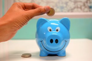 Caucasian hand holding a coin over a blue piggy bank