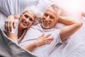 Caucasian older couple laying in bed together cuddling and smiling. 