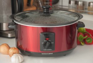 red crock pot with steam on the lid and veggies around it