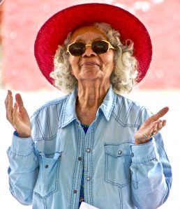 african american senior woman with a red sun hat on, jean shirt, and dark sunglasses on.