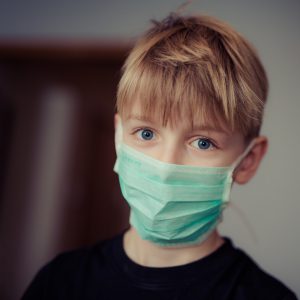 caucasian boy with blonde hair wearing a blue surgical mask.