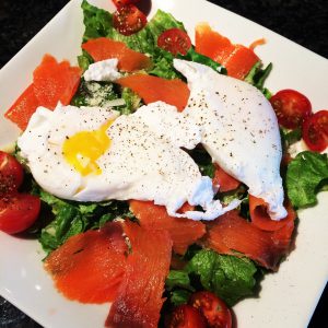 salad with lox and fried egg on top with yolk coming out.