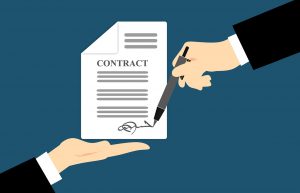 contract paper with two hands, one signing it and the other underneath it.