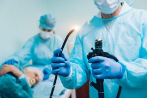 doctor in blue gown holding a black tube with a light on the end of it.