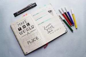 journal open with "make the world a better place" written in it with different color markers on the table next to it.