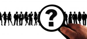 silhouette of a group of people with a magnifying glass over them with a question mark in it.