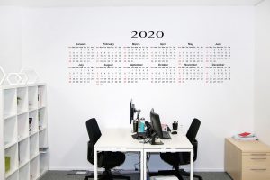 large wall calendar on the wall above a table with two black chairs.