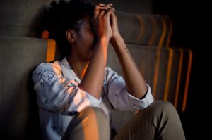 african american woman sitting with her elbows on her knees and her hands together on her forehead.