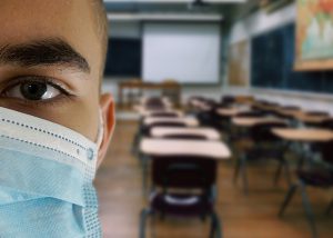 teenage boy wearing a mask with school classroom in the background.