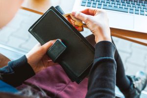 caucasian hand pulling a credit card out of a black waller while sitting in front of a laptop.